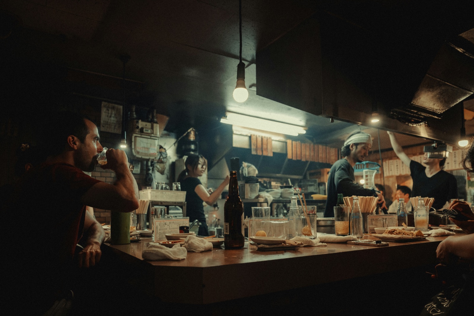 Diners at a busy counter in a lamp-lit restaurant